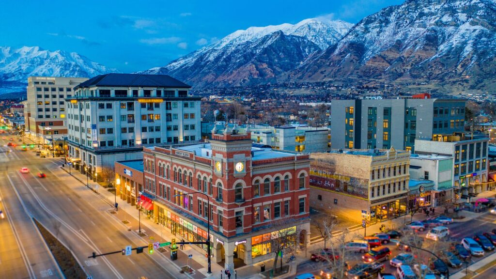 A downtown street in Utah County at dusk, with snow-covered mountains behind