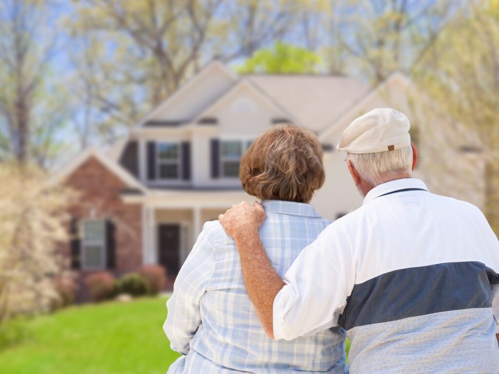 An older couple standing arm in arm, looking towards a house