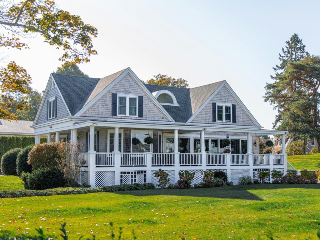 A shingled house with a wraparound porch, seen across a lawn